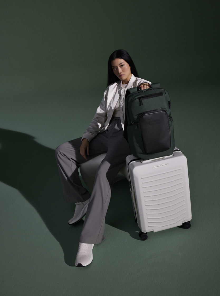 A woman sitting on a chair with a suitcase and backpack from Porsche Design.