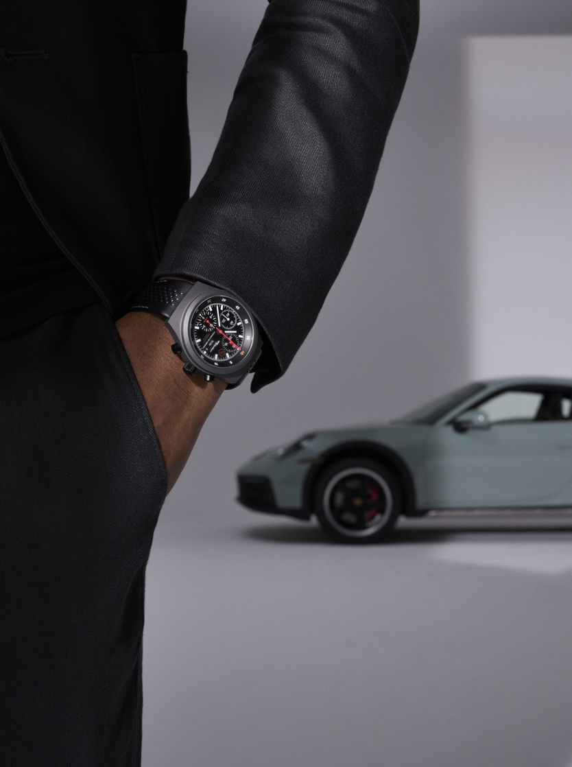 Man with porsche design timepieces watch in front of Porsche vehicle.